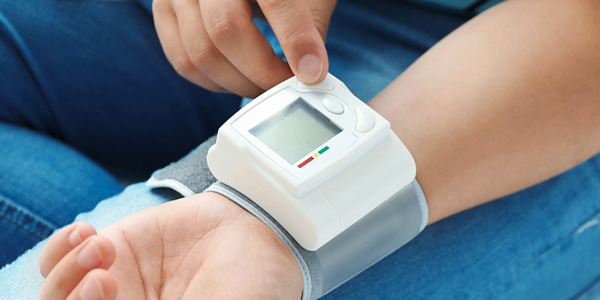 Eine Person misst mit einem elektronischen Handgelenk‑Blutdruckmessgerät den Blutdruck; ein Finger berührt die Tasten am Gerät.